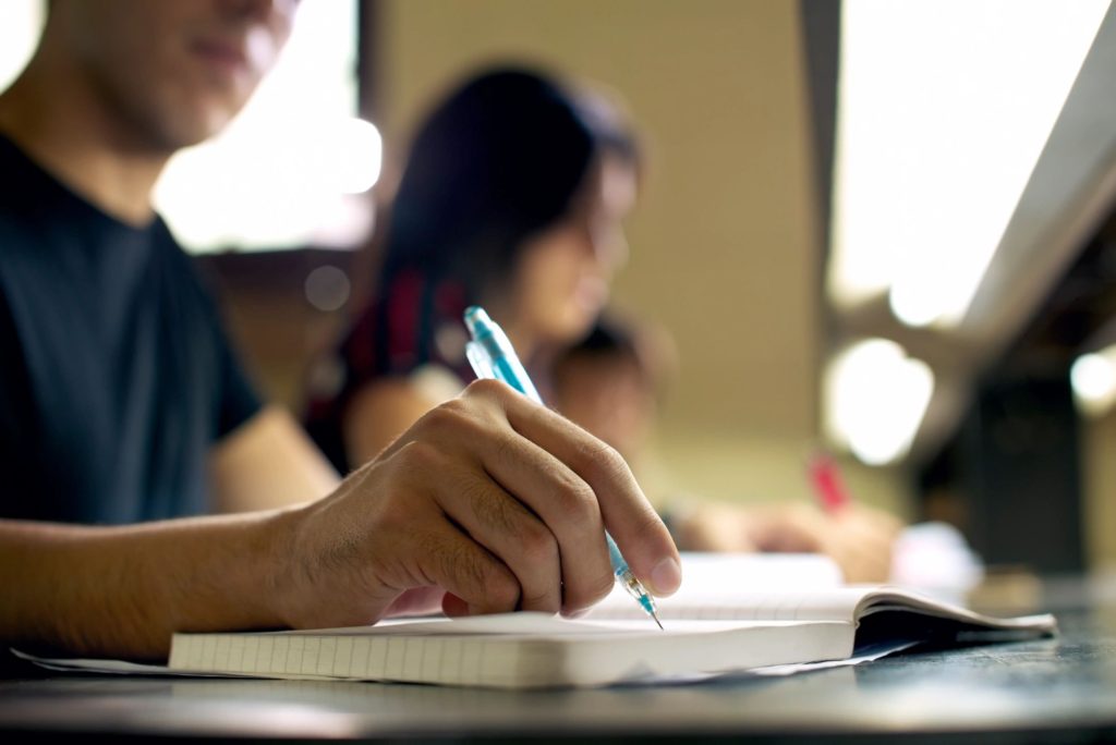 A person writing in a notebook during a class.