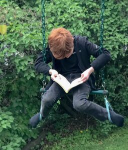 Person reading a book while sitting on a swing outdoors.