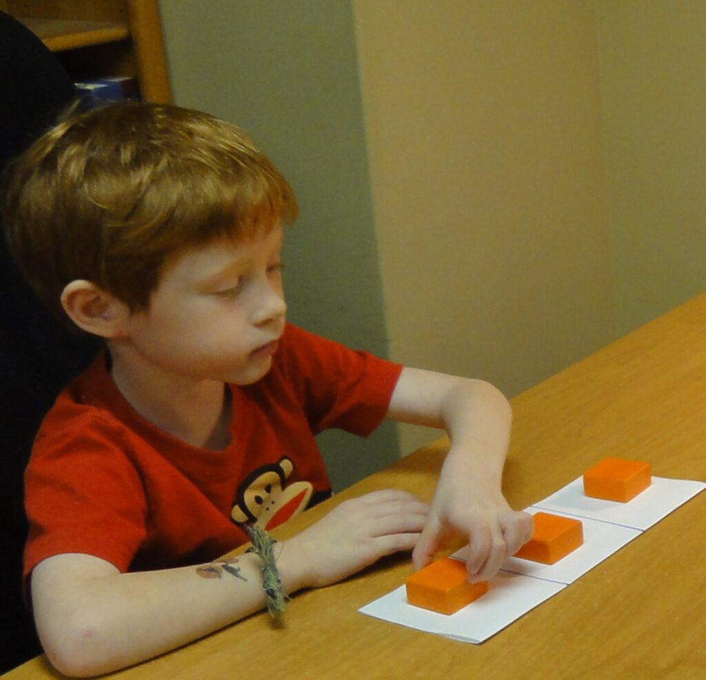 Young boy playing with orange puzzle pieces at a table.