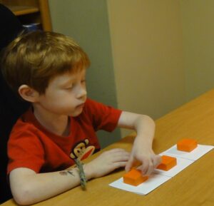 Young boy playing with orange puzzle pieces at a table.