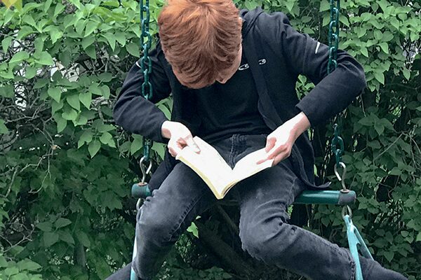 Boy Sitting On A Swing Reading Book